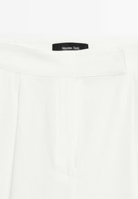 Witte katoenen broek met een platte tailleband, voorzien van een subtiele textuur en een discreete merklabel aan de bovenkant. Twee plooien aan de voorkant.