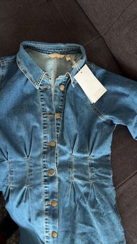 Denimkleit kraegekamarri, millel on kuldsed nupud ees, voltimisega detailid vööl ja kaasas silt. Tekstuuriga sinine kangas.