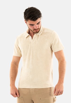 Polo shirt beige a maniche corte in morbido tessuto strutturato. Presenta un colletto classico e un logo discreto sul petto. Vestibilità casual.