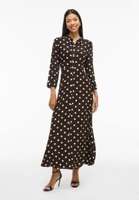 Vestido maxi de lunares marrones con cierre de botones, mangas largas y un ajuste relajado. Hecho de una tela ligera, con una textura suave.