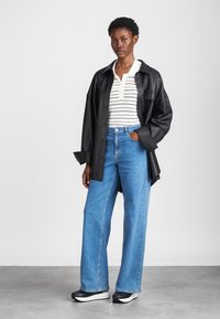 Chemise surdimensionnée en cuir noir, polo à rayures blanches, jeans droits bleu clair, baskets noir et blanc, texture lisse, coupe décontractée.