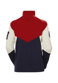 Jersey de punto con cuello alto, que presenta un diseño de tres colores en rojo, crema y azul marino, con mangas contrastantes y un parche con logotipo en el brazo.