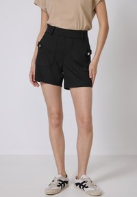 Shorts neri a vita alta in un tessuto elasticizzato, dotati di due tasche frontali con chiusura a scatto e dettagli di cucitura puliti.