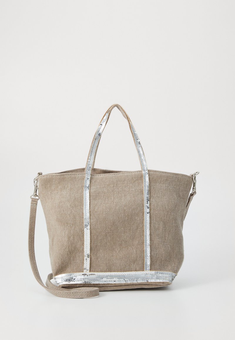 Sac en toile beige avec des accents de sequins argentés et des poignées doubles, équipé d'une fermeture zippée et d'une bandoulière amovible.