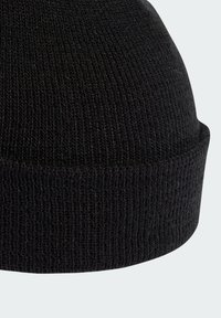 Černá pletená čepice s žebrovanou texturou. Design je těsný s ohrnutým lemem na spodní části.
