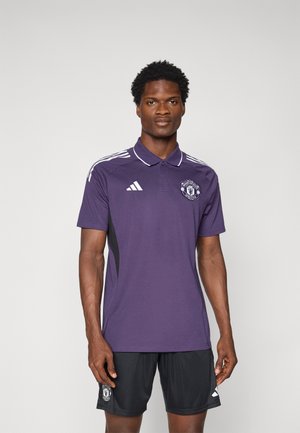 Polo athlétique violet à manches courtes, avec trois rayures blanches sur les épaules, des panneaux latéraux noirs et le logo de Manchester United sur la poitrine.