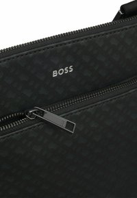 Pochette nera con texture e logo "BOSS" in argento, chiusura con zip nera, caratterizzata da un design elegante e materiale resistente.