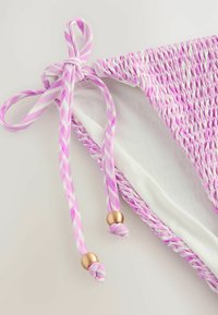 Top bikini a righe viola e bianche con texture arricciata, dotato di lacci intrecciati con perline dorate. Fodera bianca liscia visibile.