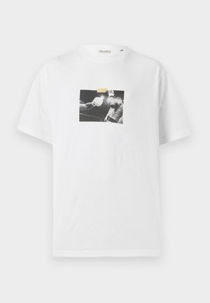 T-shirt en coton blanc avec une impression photo carré en noir et blanc d'un boxeur et un morceau de ruban jaune au-dessus de l'image. Manches courtes.