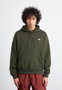 Olive green hoodie made from soft fabric, featuring a front pocket, drawstring hood, and a small white logo on the chest.