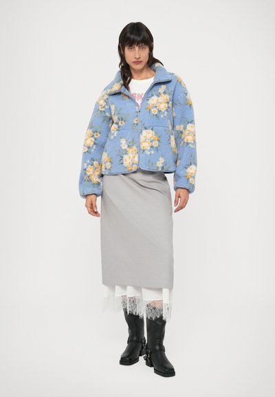 Sinine lillemustriline fliisjope luku, ümmarguse krae ja kahe eesmise taskuga. Sobitatud halli seeliku ja mustade põlviksaabastega.