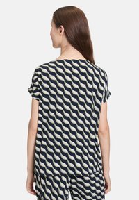 Krótki rękaw bluzki w granatowo-kremowym kolorze z falistym wzorem, wykonana z lekkiego materiału. Posiada luźny krój i zaokrąglony dół.