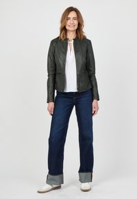 Grön läderjacka med en kort skuren passform, dragkedjestängning och sidofickor. Bärs över en vit blus och matchas med mörka jeans och sneakers.