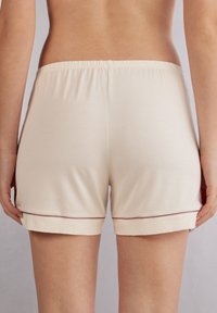 Béžové bavlněné šortky s elastickým pasem a ohrnutým lemem. Vlastnosti zahrnují jemný tmavý lem na spodním okraji. Měkká a lehká textura.