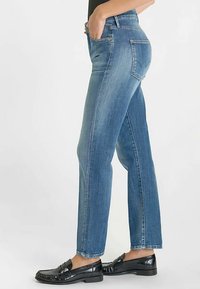 Jean en denim bleu à coupe droite, taille haute, avec un léger effet délavé. Associé à des mocassins noirs.