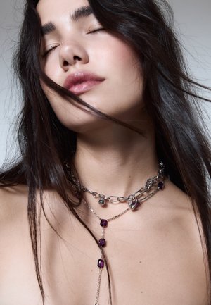 Collana metallica a strati con catene, anelli d'argento e dettagli con gemme viola. Presenta una combinazione di anelli grandi e piccoli per aggiungere texture.