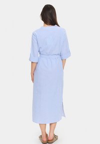 Gestreiftes blau-weißes Kleid mit Dreiviertelärmeln, tailliertem Bund und seitlichen Schlitzen. Der Stoff wirkt leicht und glatt.