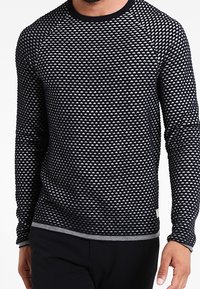 Pull à manches longues avec un motif triangulaire texturé noir et blanc, col rond, poignets et ourlet côtelés.