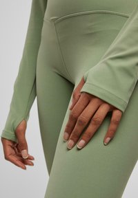 Feszes sportos szett puha világoszöld anyagból, zökkenőmentes kialakítással és hüvelykujjnak helyet adó hosszú ujjakkal, amelyek fokozzák a kényelmet és a rugalmasságot.