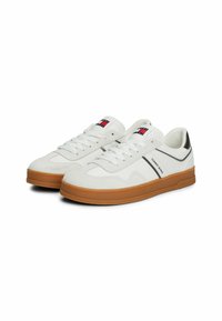 Sneakers bianchi con tomaia in pelle liscia e camoscio, dettagli neri e suola in gomma marrone. Presentano lacci e un dettaglio del logo sulla linguetta.