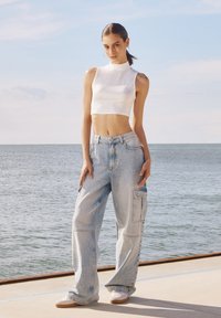 Biała krótka bluzka w połączeniu z jasnoniebieskimi luźnymi spodniami cargo. Posiada kieszenie, luźny krój oraz subtelne detale przeszycia.