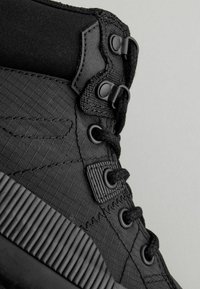 Schwarze High-Top-Sneaker mit einem strukturierten Stoffoberteil, glatten Akzenten, schwarzen Schnürsenkeln und einer gerippten Gummisohle.