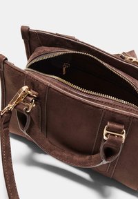 Brun ruskind håndtaske med guldfarvet hardware, der har dobbelte top håndtag og lynlåslommer. Blød tekstur med struktureret design.