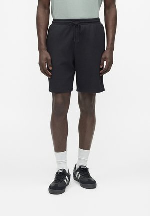 Mand iført sorte shorts med snøre, hvide ankelsokker og sorte sneakers med hvide striber, stående på hvid baggrund.