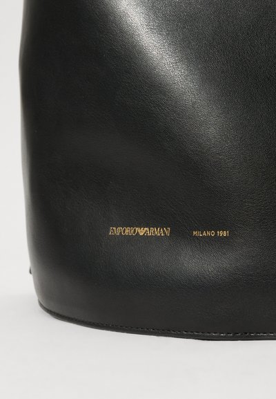 Sort læder håndtaske med en glat tekstur. Har et guld logo "EMPORIO ARMANI MILANO 1981" nær bunden. Rundet bunde design.