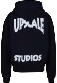 Hoodie noir avec un grand texte blanc au dos qui dit "UPSCAL" et "STUDIOS." Tissu doux avec un design classique et capuche réglable.