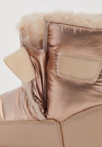 Metalické ružovo-zlaté členkové topánky s umelou kožušinou. Obsahujú mäkký béžový suchý zips a hladkú, pevnú podrážku. Viditeľné textúrované stehy.