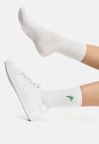 Hvid sneaker med tekstureret gummisål sammen med en hvid ribbet sok med en lille grøn palmetræ broderi.