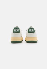 Lacoste'i tenniset valgest nahast roheliste aktsentidega; sisaldavad kollast kummist tallat ja suuri rohelisi silte kandadel tekstiga "L001."