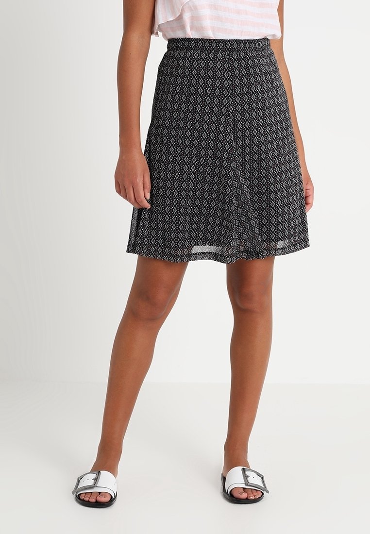 Falda negra con estampado y diseño acampanado, con cinturilla elástica, combinada con sandalias tipo chancla en blanco y negro. Tela ligera.