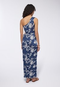 Abito maxi in tessuto blu navy con motivo floreale bianco, dotato di design a spalla unica, vita aderente e gonna fluida. Sandali visibili.