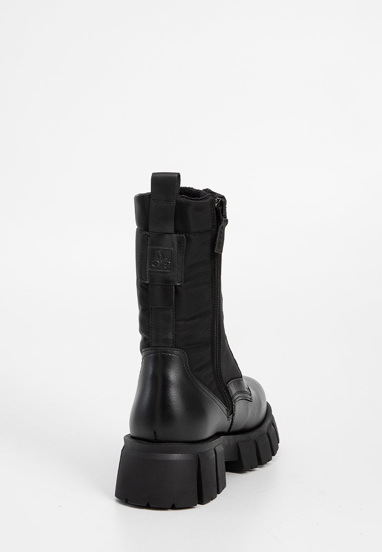 Botín negro con una combinación de cuero suave y textil duradero. Suela de goma gruesa, cremallera trasera y detalle de etiqueta de marca.