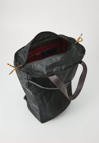 Svart nylon totebag med teksturert nettingside, rød innvendig fôr og glidelås lukking. Har justerbare stropper og fargerike glidelåser.