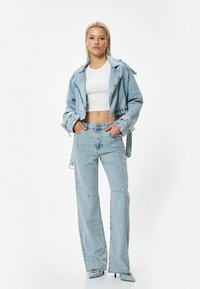 Chaqueta de denim de color azul claro con un diseño cropped, combinada con jeans de tiro alto en azul claro. Los jeans tienen un corte recto y un ligero desgaste.