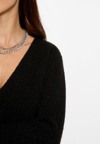 Maglione nero lavorato a maglia con una profonda scollatura a V, caratterizzato da una texture a costine. Abbinato a una collana a catena argentata multi-strato.