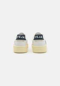Weiße Sneaker mit navyfarbenen Akzenten, Obermaterial aus strukturiertem Leder, Gummisohle und auffälligem "VEJA"-Branding an der Ferse und der Seite. Sauberes Design, minimale Details.
