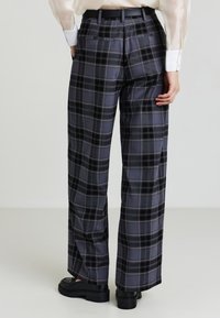 Grau kariierte weit geschnittene Hosen aus einem glatten Stoff, mit einem schwarzen Bund und Gesäßtaschen. Das Muster besteht aus schwarzen und grauen Linien.