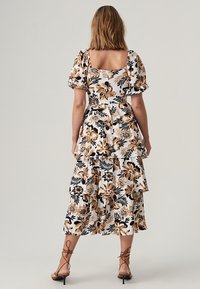Floral dress with puff sleeves, white base, black and brown flowers, tiered ruffles, and a square back detail. Finished with strappy heels.