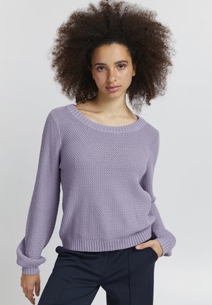 Maglione lavorato a maglia viola chiaro con una finitura testurizzata, scollatura ampia e polsini e orlo a coste. Abbinato a pantaloni scuri per creare un contrasto.