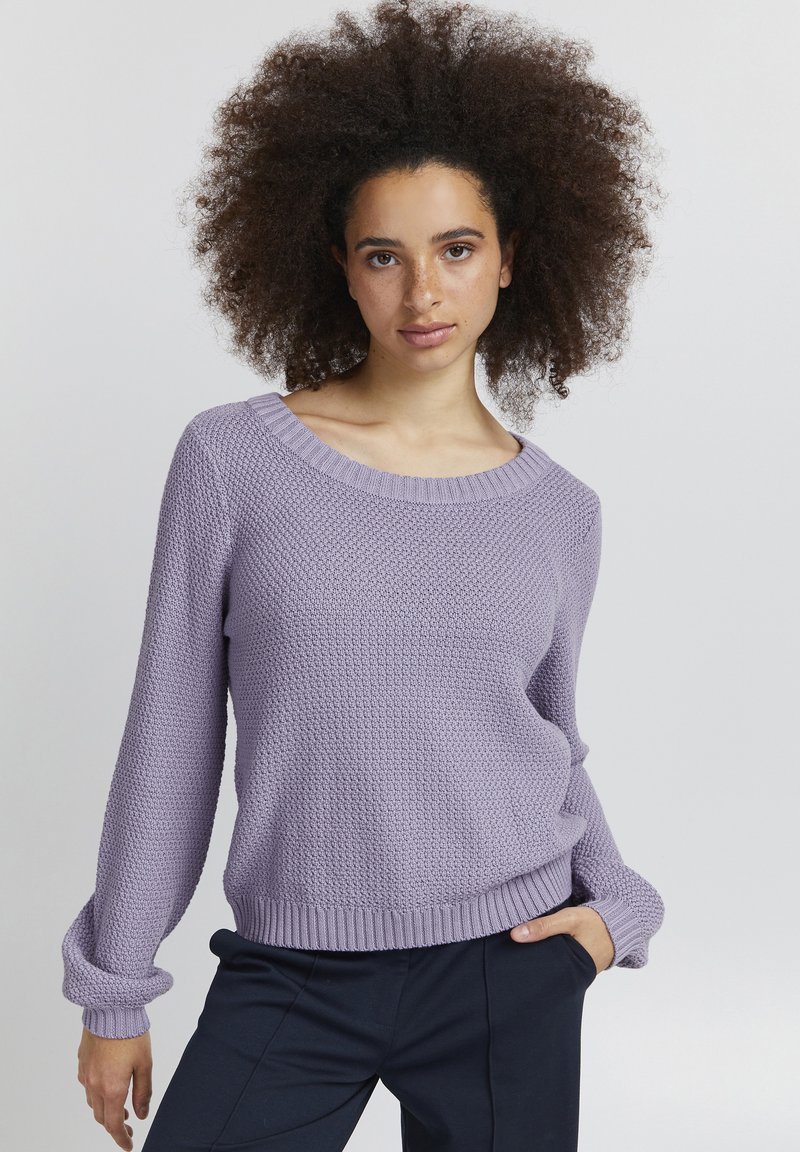 Hellblauer, gestrickter Pullover mit strukturiertem Finish, weitem Ausschnitt und gerippten Bündchen und Saum. Kombiniert mit dunkele Hosen für einen Kontrast.