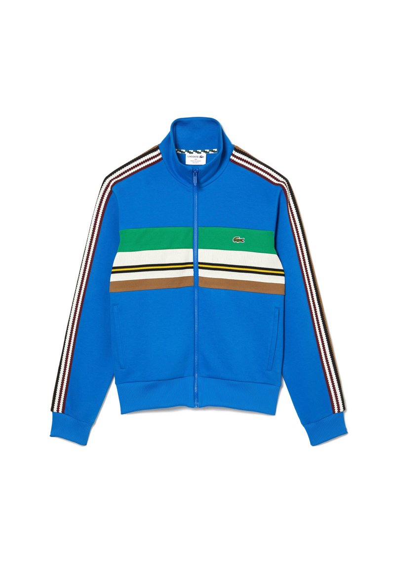 Niebieska kurtka zapinana na zamek z prążkowanymi mankietami i dołem. Posiada poziome paski w kolorach zielonym, białym, żółtym i brązowym. Logo Lacoste z przodu.