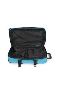 Bolsa de viaje de tela azul con interior negro; cierre con cremallera, múltiples compartimentos, dos asas y un asa retráctil.