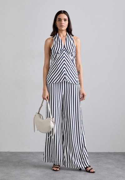 Striped halter top and wide-leg trousers in navy and white fabric, paired with a gray handbag and black strappy sandals.