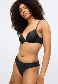 Melns krūšturis un atbilstoši bikini apakšdaļa ar gludu audumu, plānām lencēm un mežģīņu akcentiem biksīšu sānos.