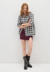 Camicia a quadri in crema e blu navy, abbinata a una gonna bordeaux con uno spacco laterale e stivali neri al ginocchio con una decorazione a fibbia.