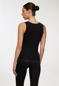 Czarny bezrękawnik o dopasowanym kroju, gładkiej fakturze i okrągłym dekolcie, w zestawieniu z czarnymi legginsami w pasującym stylu.